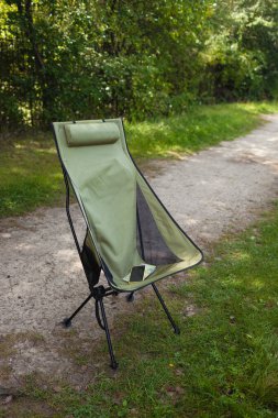 Açık havada yeşil bir kamp sandalyesine yerleştirilmiş kağıttan bir haritanın üzerinde duran bir akıllı telefonun yakın çekimi. Seyahat planlama, seyrüsefer, yürüyüş ve doğada macera kavramı.