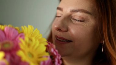 Bir buket taze sarı ve pembe Gerbera çiçeği kokan mutlu kadının yakın çekimi. Mutluluk kavramı, rahatlama, doğal güzellik ve evde özgüven..