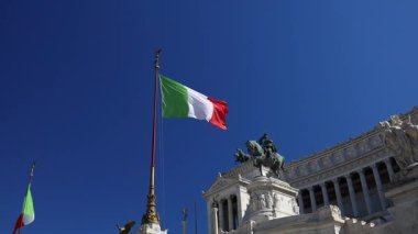 Roma 'da açık mavi gökyüzüne karşı tarihi anıtın üzerinde sallanan İtalyan ulusal bayrağı. İtalya 'nın sembolü ve ulusal kimlik şehir merkezindeki klasik mimaride sergilendi. Vatanseverlik simgesi