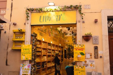 Roma, İtalya - 4 Ekim 2025: Roma 'da limonlar ve yeşilliklerle süslenmiş parlak sarı limonata dükkânı girişi içinde raflar dolusu şişe posteri ve küçük bir tadımlık alan bulunuyor.