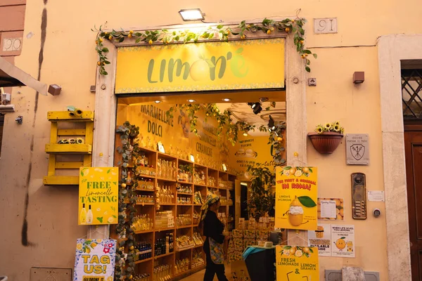 Roma, İtalya - 4 Ekim 2025: Roma 'da limonlar ve yeşilliklerle süslenmiş parlak sarı limonata dükkânı girişi içinde raflar dolusu şişe posteri ve küçük bir tadımlık alan bulunuyor.