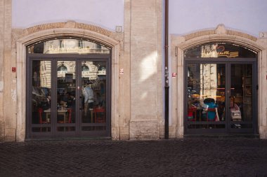 Roma 'nın tarihi merkezinde büyük cam kapıları olan bir kafe. İtalya, sıcak iç ışık ve Avrupa' nın klasik kentsel atmosferini kaldırım taşı bir sokakta gösteriyor..