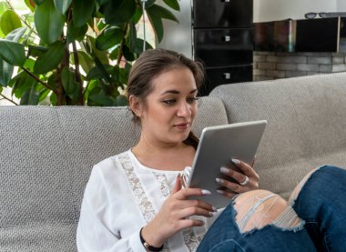 Beyaz bluzlu ve tabletli kot pantolonlu güzel bir kız. İş, internet üzerinden iletişim, online alışveriş, gazete okumak.