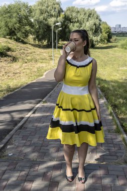 Parkta bir fincan kahveyle şık elbiseli güzel bir kızın portresi, mutlu ve gülümseyen bir kadın.