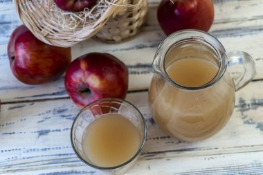 Sepetteki kırmızı elmalar ve tahta masadaki sürahide elma suyu.