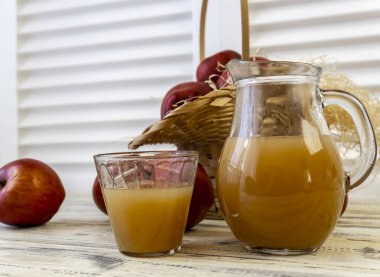 Sepetteki kırmızı elmalar ve tahta masadaki sürahide elma suyu.