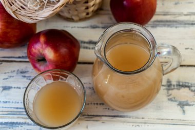 Sepetteki kırmızı elmalar ve tahta masadaki sürahide elma suyu.