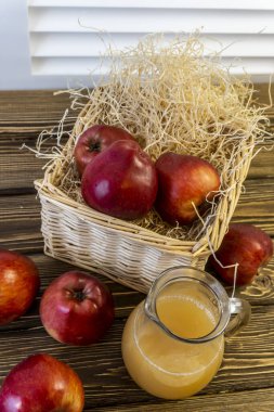 Sepetteki kırmızı elmalar ve tahta masadaki sürahide elma suyu.