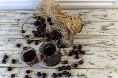 Kiraz ve kiraz suyu veya ahşap bir masada şarap, bir sürahi ve meyve suyu dolu bir bardak, kirazlı bir sepet.