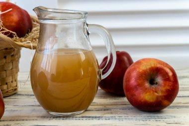 Sepetteki kırmızı elmalar ve tahta masadaki sürahide elma suyu.