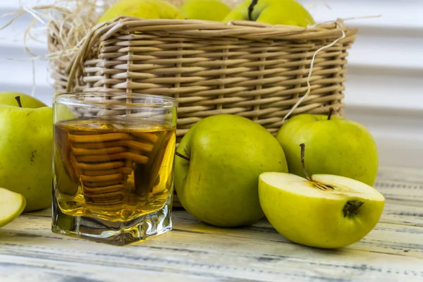 Green apples, glass with apple juice and basket with apples on wooden background