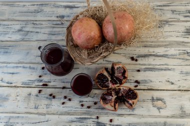 Narlar sepetin içinde ve masanın üzerinde tahta bir arka planda. Sürahi ve bardakta nar suyu.