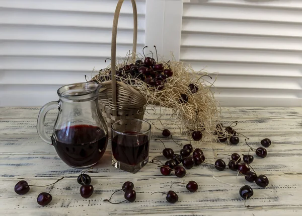 樱桃和樱桃汁或葡萄酒放在木制桌子上 酒壶和杯子里有果汁 篮子里有樱桃 — 图库照片