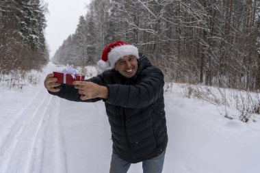Noel Baba şapkalı bir adam ve kışın ormanda bir Noel hediyesi.