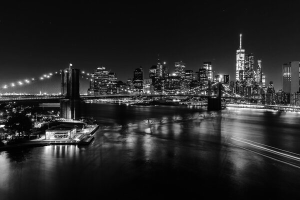 Black and white picture of the skyline of downtown Manhattan with Brooklyn Bridge and East River in New York City at night