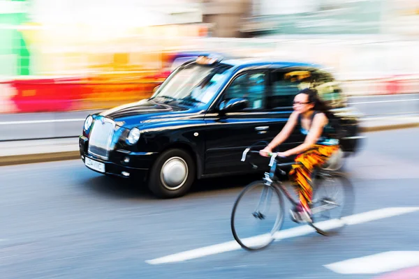 Велосипедист и лондонское такси в движении размыты в городском движении Лондона, Великобритания — стоковое фото
