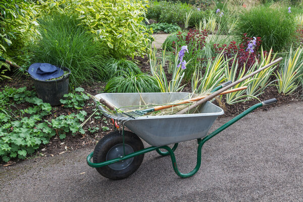 Тачка с другими садовыми инструментами в саду
