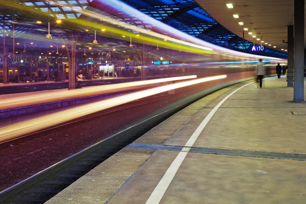 Vista notturna di un treno di passaggio in movimento sfocato in una stazione ferroviaria — Foto Stock