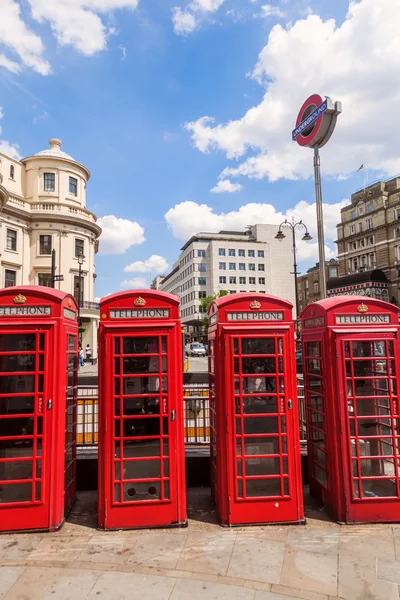 Cuatro cabinas telefónicas rojas tradicionales seguidas en Londres con un cartel de metro en Londres, Reino Unido — Foto de Stock