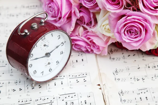 Old alarm clock, pink roses and notes — Stock Photo, Image