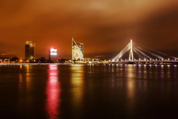 Panorama nocturno de Riga, Letonia, con el puente Vansu sobre el Daugava y rascacielos modernos — Foto de Stock