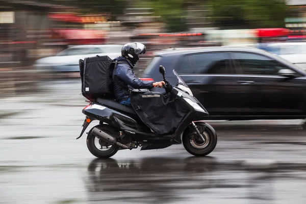 Скутерист в движении размыт на мокрой улице в городском движении — стоковое фото