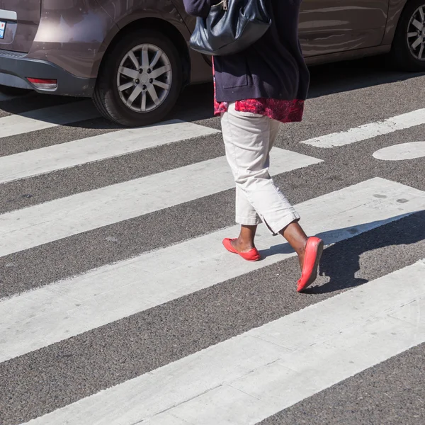 Женщина, идущая по пешеходному переходу, пока мимо проезжает машина — стоковое фото