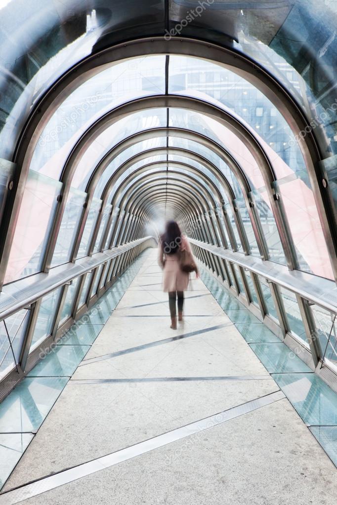 Business woman walking on a glass roofed footbridge