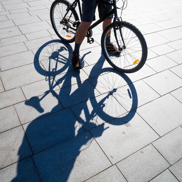 Cycliste debout sur une place avec de longues ombres — Photo
