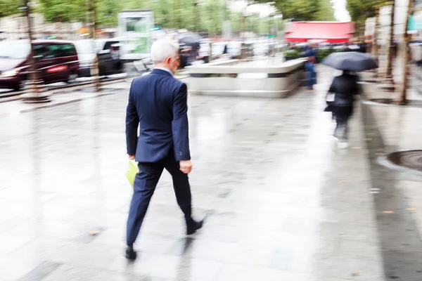 Бизнесмен, гуляющий по дождливому городу в движении, размыт — стоковое фото