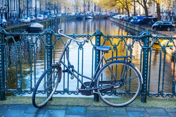 Fiets leunend op een leuning van een kanaal brug in Amsterdam, Nederland — Stockfoto