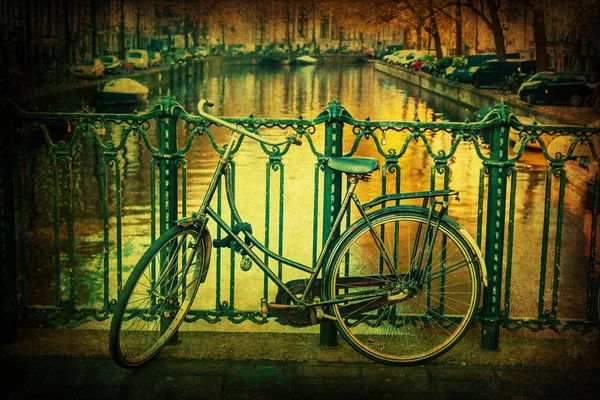 Картина в винтажном стиле с велосипедом, опирающимся на перила моста через канал в Амстердаме, Нидерланды — стоковое фото