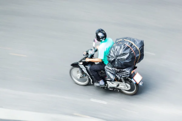 Cavaliere ciclomotore con un grande sacchetto di plastica sulla sfocatura in movimento — Foto Stock