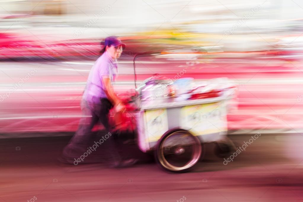 Thai woman with a mobile cook shop on a handcart, shown in creative motion blur