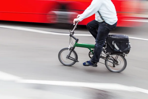 Hombre de negocios con una bicicleta plegable en el tráfico de la ciudad en desenfoque movimiento — Foto de Stock