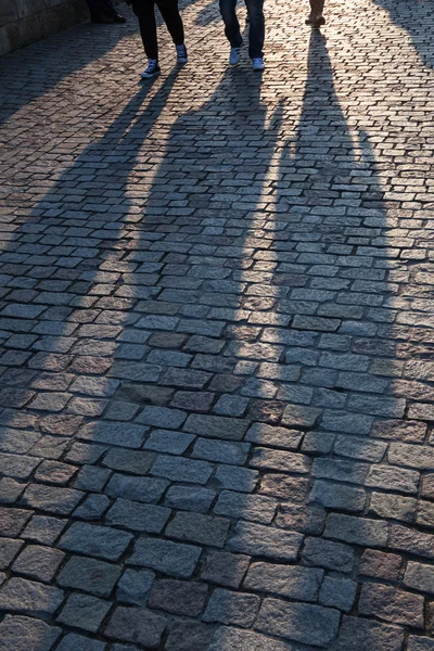 Långa skuggor av människor på en kullersten trottoar — Stockfoto