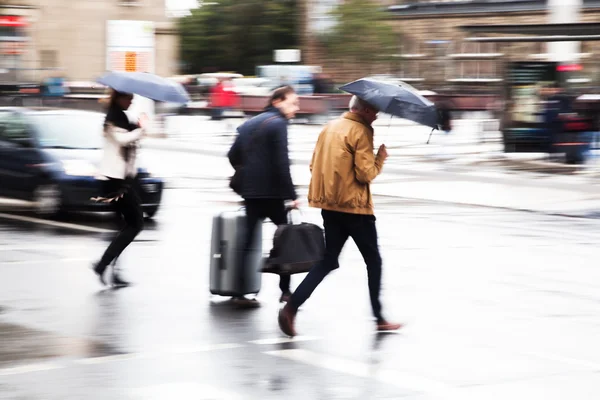 People with umbrellas in motion blur crossing a street in the rainy city