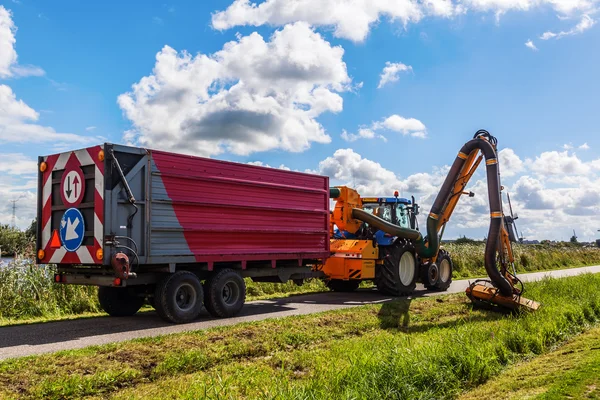 Ciągnik z kosiarka w akcji o słynne wiatraki w Kinderdijk, Holandia — Zdjęcie stockowe