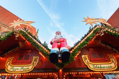 Santa Claus sitting on a stall of a Christmas Market clipart