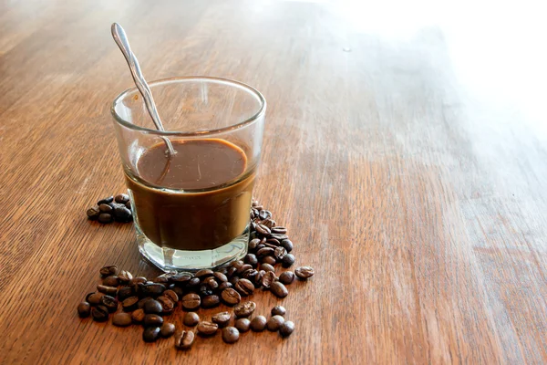 Tmavá horká káva a semen na dřevěný stůl — Stock fotografie