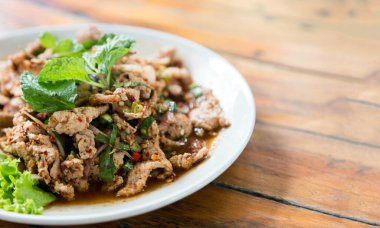 Baharatlı domuz eti, otla kaynatılmış ve ahşap masada kanlı sos servis ediliyor.