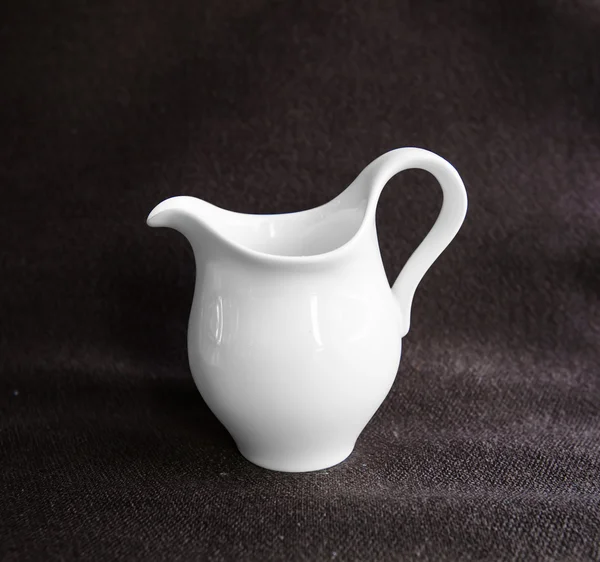 Cerrar olla de leche de cerámica blanca sobre fondo de tela marrón —  Fotos de Stock
