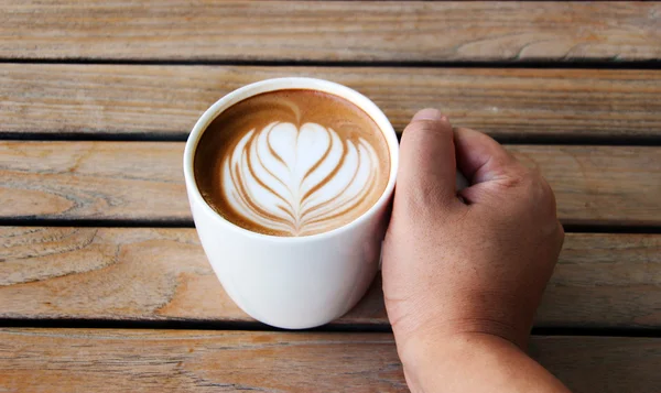 Ręka trzymać się kawa filiżanki sztuka latte — Zdjęcie stockowe