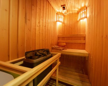 Modern empty wooden sauna room with warm lighting, stacked rocks on the heater, and wooden accessories. Perfect for wellness, spa, and relaxation concepts