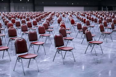 Geniş bir konferans salonunda sıralar dolusu boş kırmızı sandalye, büyük bir iş toplantısı ya da kurumsal etkinlik düzenlenmesini düzgünce düzenlenmiş ve bekliyor.