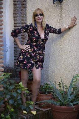 Çiçekli mini bir elbise ve güneş gözlüğü takan bir kadın saksı bitkilerinin arasında güvenle poz veriyor.