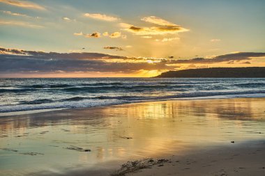 Okyanusun üzerinde güneş batıyor ve kumlu sahilde dalgalar kıyıya vuruyor.