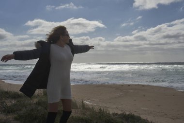 Vahşi bir sahilde kollarını açmış, kendini özgür hisseden bir kadın.