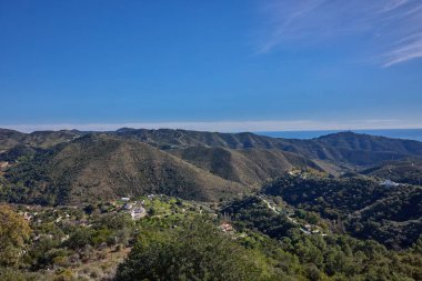 Parlak mavi gökyüzünün altında dağınık evleri olan yuvarlanan tepeler ve vadiler