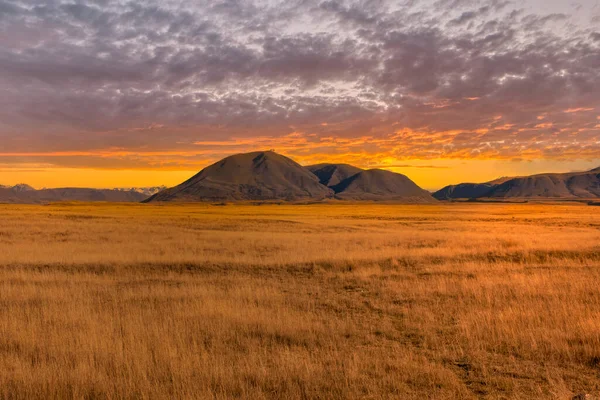 The mountains and dry tussock covered valley floor at Hakatere Conservation park in the Ashburton Highlands under a vibrant sunset sky